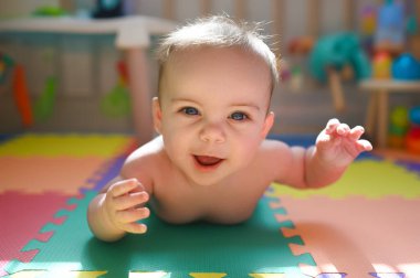 Sevimli, sevimli, mutlu, bebek bezli bebek bebek, bebek odasında oyuncaklarla birlikte gelişmekte olan köpük bir bulmaca minderinde yerde sürünüyor ve oynuyor. Sağlıklı çocuk konsepti. Bebek eşyaları ambalajı