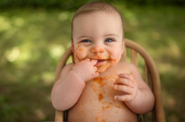 Şirin, sevimli, sevimli, komik, pis bebek yüzüne sürülmüş meyve ya da sebze püresi ile kendini yemeye çalışıyor. Bebekler ilk katı yiyeceği tamamlar. Organik doğal malzemeler. Açık havada yaz