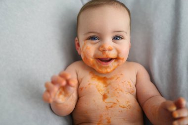 Şirin, sevimli, sevimli, komik, pis bebek yüzüne sürülmüş meyve ya da sebze püresi ile kendini yemeye çalışıyor. Bebeklerin ilk tamamlayıcı yemeği. Organik doğal malzemeler. Bebek maması konsepti