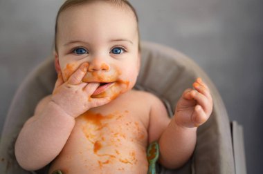 Şirin, sevimli, sevimli, komik, pis bebek yüzüne sürülmüş meyve ya da sebze püresi ile kendini yemeye çalışıyor. Bebeklerin ilk tamamlayıcı yemeği. Organik doğal malzemeler. Bebek maması konsepti