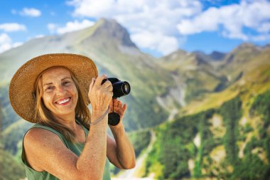Gülümseyen mutlu, yaşlı bir turistin portresi. Elinde kamerayla dağların arkasına poz veriyor. Kırsalda çimlerin üzerinde saman şapkalı zarif bir bayan. Aktif emekliler konsepti