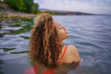 Çekici mutluluk artı boyut Afro-Amerikan siyahi kadın açık havada deniz gölü suyunda su sıçratarak yüzmeyi seviyor.