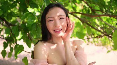 Açık hava portresini kapat. Güzel Çinli genç Asyalı kadın. Mükemmel cilt, güneşli yaz günü yeşil yaprakların önünde poz veriyor. Doğal yüz tedavisi. Kozmetoloji, cilt bakımı ve spa. Fragnance konsepti