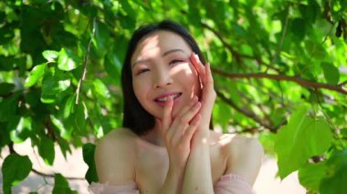 Açık hava portresini kapat. Güzel Çinli genç Asyalı kadın. Mükemmel cilt, güneşli yaz günü yeşil yaprakların önünde poz veriyor. Doğal yüz tedavisi. Kozmetoloji, cilt bakımı ve spa. Fragnance konsepti