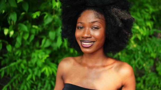 スローモーションの肖像画を閉じる美しい若いアフリカ系アメリカ人黒人女性完璧な白い歯は外で笑みを浮かべて 晴れた夏の日の緑の葉 顔の治療 スキンケア — ストック動画