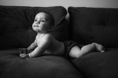 Koyu gri lacivert koltukta düz kollarında oturan tatlı, duygusal gülümseyen komik çocuk. Bebek yüz ifadeleri. Sağlıklı bir çocuk. Ev konforlu mobilyalar, mutlu aile konsepti. 