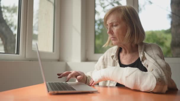 Старшая Пожилая Женщина Работающая Дома Ноутбуком Сломанной Рукой Закрытом Помещении — стоковое видео