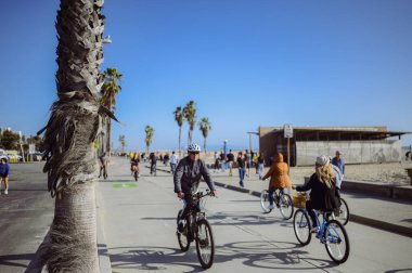 10 Mart 2024, Los Angeles, ABD. Venedik plajı güneşli bir günde. Yaya geçidi boyunca yürüyen turist kalabalığı var. Bisikletçiler bisiklet yolunda gezerler. Güzel okyanus manzarası