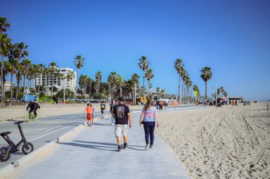 10 Mart 2024, Los Angeles, ABD. Venedik plajı güneşli bir günde. Yaya geçidi boyunca yürüyen turist kalabalığı var. Bisikletçiler bisiklet yolunda gezerler. Güzel okyanus manzarası