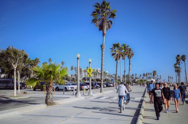 10 Mart 2024, Los Angeles, ABD. Venedik plajı güneşli bir günde. Yaya geçidi boyunca yürüyen turist kalabalığı var. Bisikletçiler bisiklet yolunda gezerler. Güzel okyanus manzarası