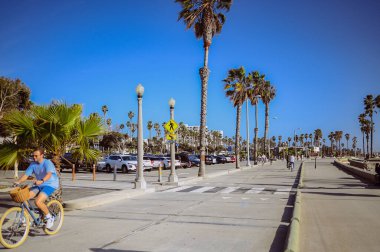 10 Mart 2024, Los Angeles, ABD. Venedik plajı güneşli bir günde. Yaya geçidi boyunca yürüyen turist kalabalığı var. Bisikletçiler bisiklet yolunda gezerler. Güzel okyanus manzarası
