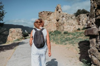 Yaşlı, gülümseyen, yaşlı, gezgin, olgun, sırt çantalı bir turist eski Avrupa kalelerinde poz veriyor. Emekli insanlar yaz tatili, aktif yaşam tarzı konsepti