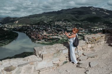 Olgun kadın turist, Gürcistan 'ın Mtskheta kentindeki Aragvi ve Kura nehirlerinin kesiştiği yerde fotoğraf çekiyor. Emekli insanlar yaz tatili, aktif yaşam tarzı konsepti. 