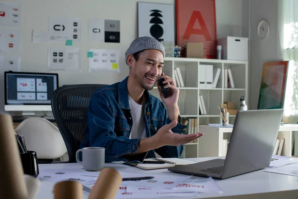 Asian man Graphic designer talking on mobile phone while working in office. Artist Creative Designer Illustrator Graphic Skill Concept.