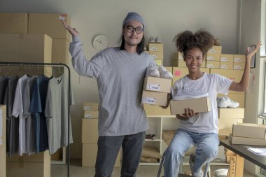 Confident mixed race young couple of Asian man and african-american woman retail seller, entrepreneur, online store drop shipping small business owner looking at camera in delivery shipping warehouse