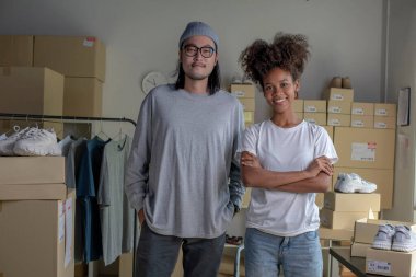 Confident mixed race young couple of Asian man and African-American woman retail seller, entrepreneur, online store drop shipping small business owner looking at camera in delivery shipping warehouse