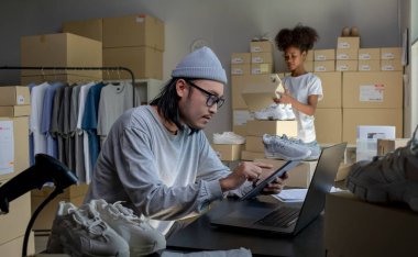 Mixed race couple of Asian man and African-American woman online seller confirming orders from customer on laptop and tablet computer.