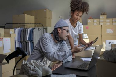 Mixed race couple of Asian man and African-American woman online seller confirming orders from customer on laptop and tablet computer.