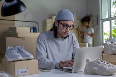 Mixed race couple of Asian man and African-American woman online seller confirming orders from customer on laptop computer.