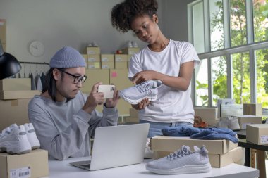Mixed race couple of Asian man and African-American woman online seller confirming orders from customer on laptop computer.