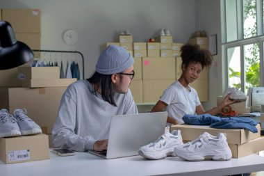 Mixed race couple of Asian man and African-American woman online seller confirming orders from customer on laptop computer.