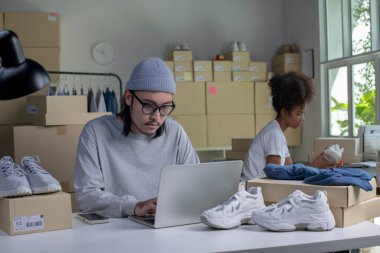 Mixed race couple of Asian man and African-American woman online seller confirming orders from customer on laptop computer. 