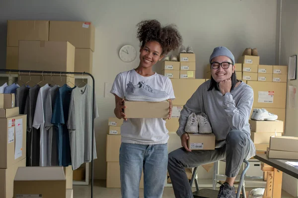 Confident mixed race young couple of Asian man and african-american woman retail seller, entrepreneur, online store drop shipping small business owner looking at camera in delivery shipping warehouse