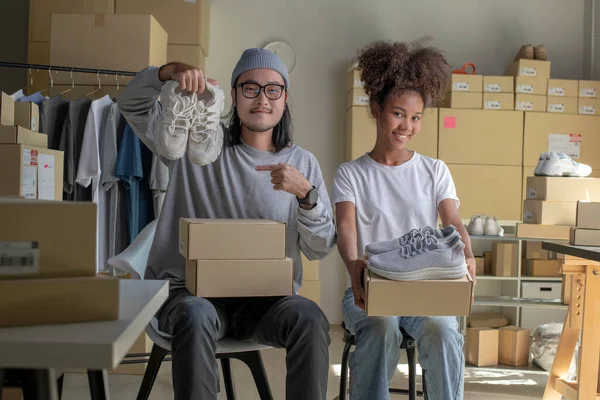 Confident mixed race young couple of Asian man and African-American woman retail seller, entrepreneur, online store drop shipping small business owner looking at camera in delivery shipping warehouse