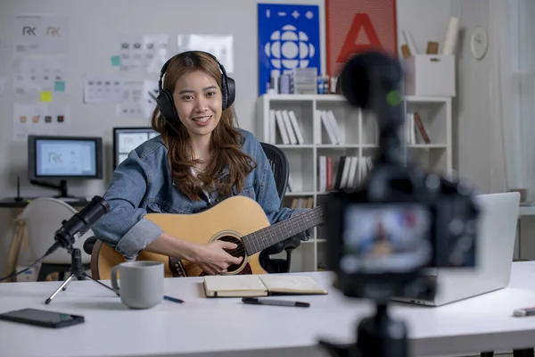 Young Asian female graphic designer blogger influencer playing guitar while shooting education tutorial vlog training filming video course for social media at studio.