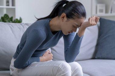 Genç Asyalı kadın evdeki kanepede otururken karın ağrısı çekiyor. Hasta kadının midesi ağrıyor..