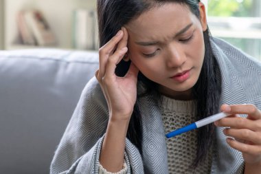 Depresyondaki genç Asyalı kadın elinde negatif ya da pozitif hamilelik testi tutuyor..