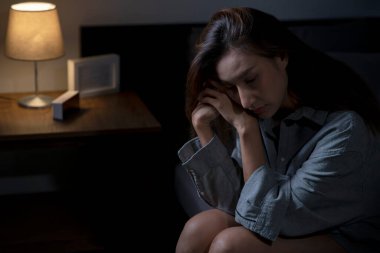 Yatak odasındaki genç Asyalı kadın üzgün, yorgun ve endişeli, akıl sağlığı bozuk, yatakta oturan kadın uykusuzluktan uyuyamıyor..