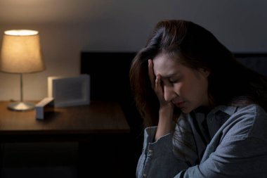 Yatak odasındaki genç Asyalı kadın üzgün, yorgun ve endişeli, akıl sağlığı bozuk, yatakta oturan kadın uykusuzluktan uyuyamıyor..