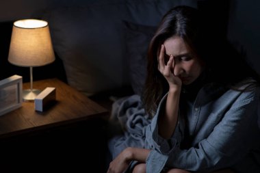 Yatak odasındaki genç Asyalı kadın üzgün, yorgun ve endişeli, akıl sağlığı bozuk, yatakta oturan kadın uykusuzluktan uyuyamıyor..