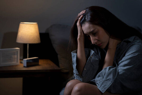 Young Asian woman in bedroom feeling sad tired and worried suffering depression in mental health, woman sitting in bed cannot sleep from insomnia.