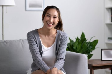 Evdeki kanepede oturan mutlu ve çekici Asyalı kadının portresi.