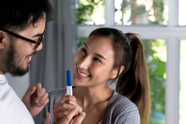 Mutlu Asyalı çift evdeki oturma odasında hamilelik testini kontrol ediyor.