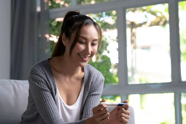 Молодая Азиатка Проводит Домашний Тест Беременность Выглядит Счастливой Гостиной — стоковое фото