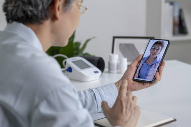 Oturma odasında doktoruyla çevrimiçi görüşme yaparken akıllı telefonlu Asyalı bir kadın. Teletıp konsepti.