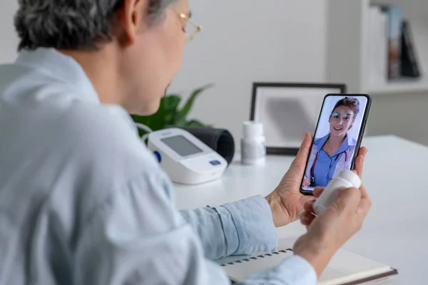 在客厅与医生进行在线咨询时 亚洲妇女使用智能手机 远程医疗的概念 免版税图库图片