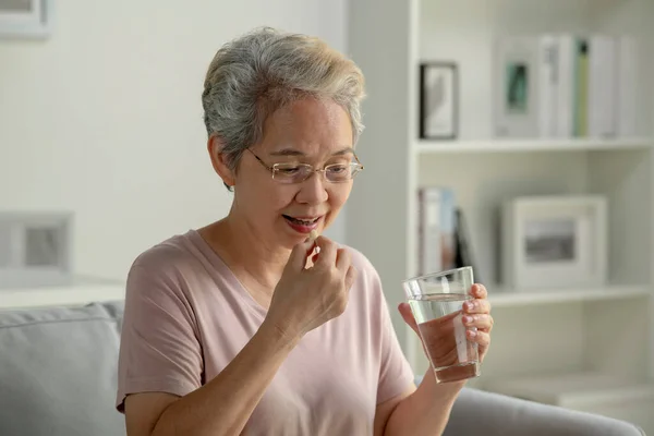 亚洲老年妇女在家里 保健和人的观念中吃药 图库照片