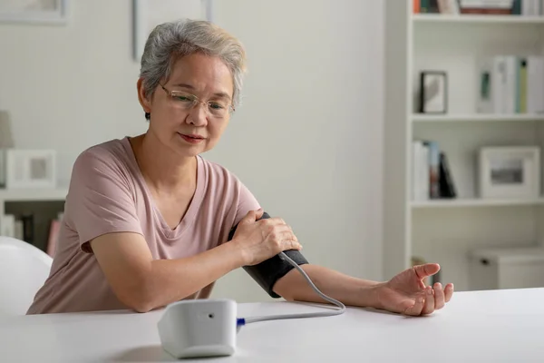 亚洲老年妇女在家测量血压 图库图片
