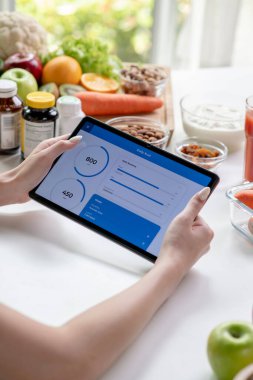 Masada çeşitli meyve, fındık, sebze ve beslenme malzemeleri bulunan tabletten veri toplayan profesyonel kadın beslenme uzmanı.