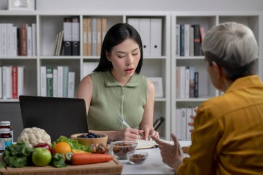 Ofisteki tıbbi konsültasyon sırasında yemek planı ve sağlıklı ürünlerden bahseden kadın müşteriyle beslenme uzmanı.