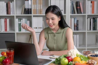 Sofrada çeşitli meyve, fındık, sebze ve beslenme maddeleri bulunan Asyalı kadın müşterisine laptopta danışmanlık yapıyor.