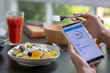 Yemek yerken telefonundaki kalori ve besin uygulamalarını kontrol eden bir kadın. Profesyonel Beslenme Uzmanı.