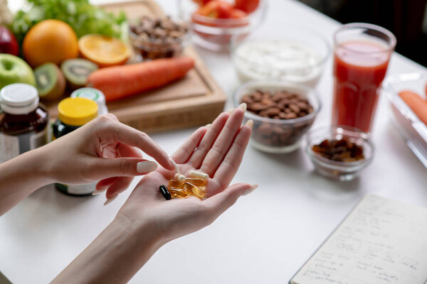 Woman professional nutritionist checking dietary supplements in hand, surrounded by a variety of fruits, nuts, vegetables, and dietary supplements on the table