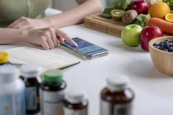 stock image Woman professional nutritionist working and checking data from a smartphone with a variety of fruits, nuts, vegetables, and dietary supplements on the table