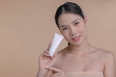 Genç Asyalı bir kadının portresi. Elinde reklam metni için bej arka planda bir model ürünle gülümsüyor. Cilt için sağlık hizmeti kavramı, reklam için güzellik ürünleri.