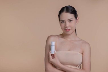 Genç Asyalı bir kadının portresi. Elinde reklam metni için bej arka planda bir model ürünle gülümsüyor. Cilt için sağlık hizmeti kavramı, reklam için güzellik ürünleri.
